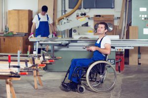 disabled worker in wheelchair in a carpenter's workshop with his colleague